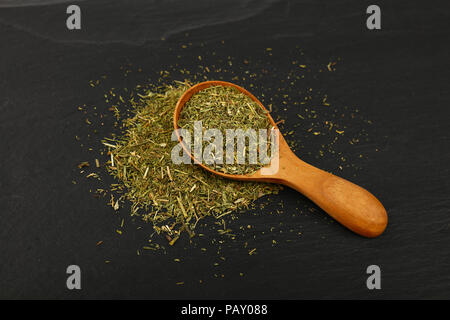 Schließen Sie einen hölzernen Schaufeln Löffel voller grüner getrocknete Kräuter, Dill oder majoran auf dem Hintergrund der schwarzen Schiefer, hohe Betrachtungswinkel Stockfoto