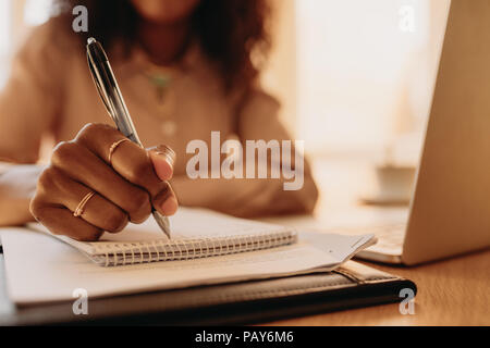 Geschäftsfrau am Laptop zu Hause sitzen. Nahaufnahme der Hand einer Frau mit Stift und schreiben auf Notepad. Stockfoto