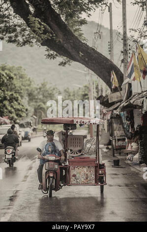 Eis Verkäufer mit einem Kind, einem motorisierten Dreirad im Regen Kanchanaburi Thailand Stockfoto