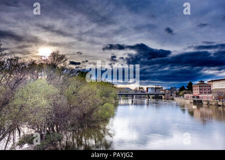 Sonnenuntergang auf dem Ebro durch Logroño mit einem bewölkten Himmel und einer Brücke im Hintergrund Stockfoto