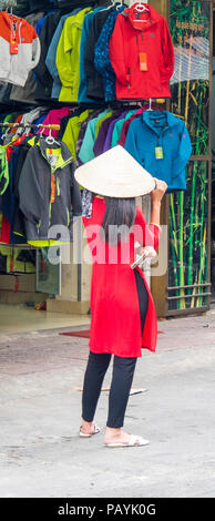 Rückansicht eines vietnamesischen Frau trägt ein rotes Oberteil und ein Stroh konische hat vor ein Geschäft mit Jacken in Ho Chi Minh City, Vietnam. Stockfoto