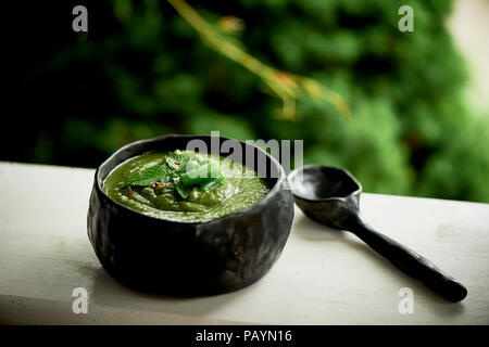 Suppe püriert grünes Gemüse, Brokkoli, Bohnen, Erbsen. Dunkle Geschirr handgefertigt in einem rustikalen Stil von Ton. Vegetarisches Essen. Nahaufnahme Stockfoto