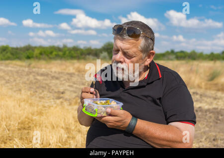 Bärtige senior ist bereit für eine gesunde Ernährung (gedünstetes Gemüse) im Freien Stockfoto