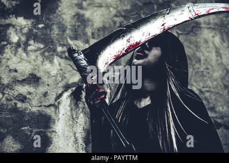 Hexe lecken Blut auf Reaper. Weiblicher Dämon Engel in schwarzer Kleidung und Haube auf grunge Wand Hintergrund. Halloween Tag und Geheimnis, das Konzept. Fantasie von m Stockfoto