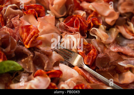 Nahaufnahme der verschiedenen Arten von italienischen Fleisch (ham) auf einem Teller mit der Gabel und ein Blatt Basilikum Stockfoto