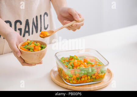 Schöpfkelle aus gedämpftem frisch geernteten jungen Gemüse, einschließlich Crinkle cut geschnittene Karotten, Erbsen und Kartoffeln für eine gesunde Begleitung zum Abendessen Stockfoto