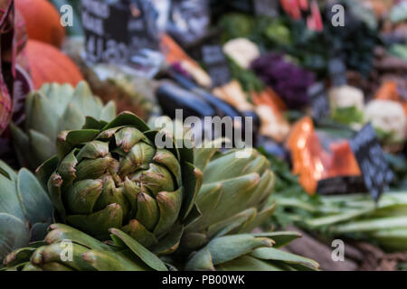 Eine Artischocke Isoliert gegen eine backgdrop von anderen frischen Gemüse auf Verkauf in der London Borough Market, Großbritannien Stockfoto