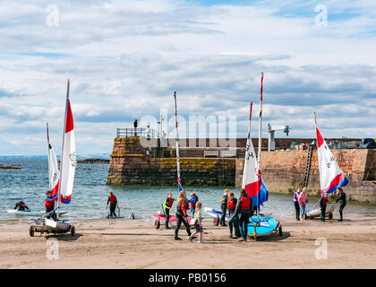 Yacht Club mit Menschen ziehen Jollen aus Meer auf Anhänger an der West Bay Beach mit Hafen Wand- und Eingang, North Berwick, East Lothian, Schottland, Großbritannien Stockfoto