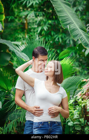 Portrait von zwei Menschen, Mann Frau Mädchen zusammen, unter grünen Bäumen, Pflanzen im Park außerhalb, Lächeln, Lachen, umarmen, wegsehen, intime m Stockfoto