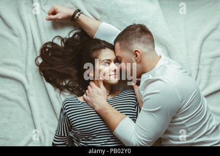 Portrait von wunderschönen, romantischen junges Paar Mann Frau in Liebe umarmen, küssen, liegend auf dem Boden auf weißen Teppich Teppich in Innenräumen zu Hause, getönt mit Filtern Stockfoto