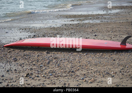 Red Surf Board Festlegung anfällig auf einem felsigen Strand. Stockfoto