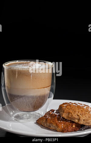 Kaffee und Kekse. Cappuccino doppelwandige Glas Becher, mit hausgemachten Kekse. Nahaufnahme auf schwarzem Hintergrund mit kopieren. Stockfoto