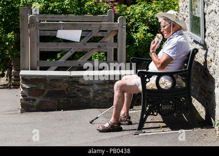 Ein reifer Urlauber, der in Weiß gekleidet ist und die Sonne und ein Eis in Newquay Cornwall genießt. Stockfoto