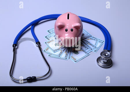 Sparschwein mit Dollar Noten und Stethoskop auf einem Schreibtisch aus Holz. Stockfoto
