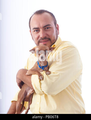 Studio Portrait auf einen weißen Hintergrund von einem Mann in einem gelben Hemd, mit einem Chihuahua Hund in seine Arme Stockfoto