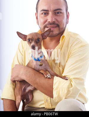 Studio Portrait auf einen weißen Hintergrund von einem Mann in einem gelben Hemd, mit einem Chihuahua Hund in seine Arme Stockfoto