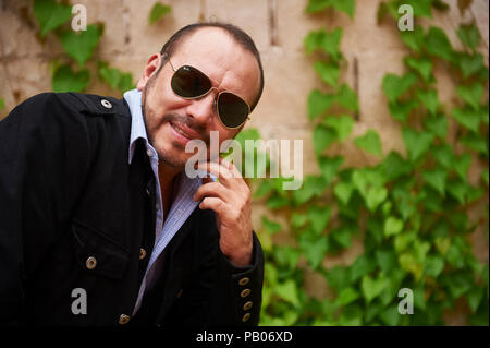 Ein Mann stellt Outdoor, tragen, Sonnenbrille grün, blau karierte Hemd und eine schwarze Jacke Stockfoto