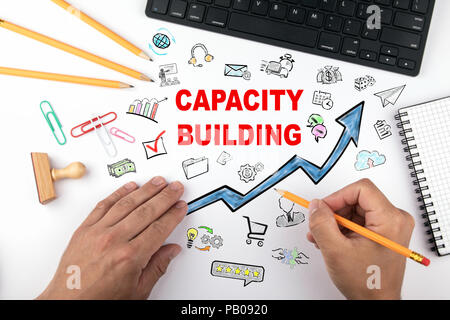 Capacity Building Konzept. Blauer Pfeil und Symbole rund um. Hände auf Schreibtisch Tun des Geschäfts Stockfoto