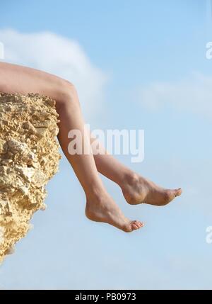 Woman's Beine über den Rand eines Rock baumelt. Stockfoto