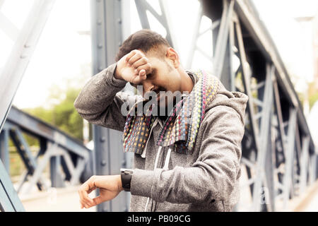 Jogger stehen auf einer Fußgängerbrücke mit der Hand auf seinen Kopf, schaut auf seine Uhr Stockfoto