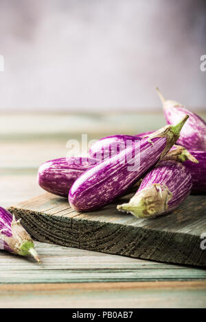 Haufen kleine Aubergine oder Aubergine Gemüse mit basilikumblätter auf alten Holz- Hintergrund. Gesunde Ernährung Konzept mit kopieren. Stockfoto