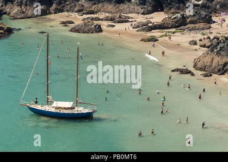 Sommer in Cornwall - Urlauber an Kynance Cove auf der Lizard Halbinsel paddeln Um eine Yacht Strände bei Ebbe, Großbritannien Stockfoto