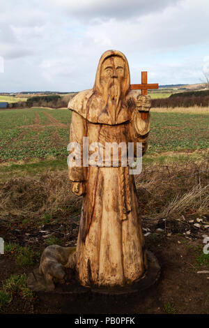 Geschnitzte Holzfigur, die St Cuthbert auf St Cuthbert's Way darstellt, einem Fußweg in der Landschaft von Northumberland, England. Stockfoto