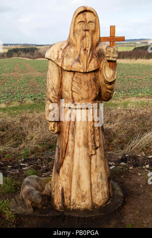 Geschnitzte Holzfigur, die St Cuthbert auf St Cuthbert's Way darstellt, einem Fußweg in der Landschaft von Northumberland, England. Stockfoto