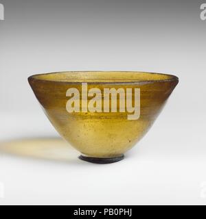 Glas konische Schüssel. Kultur: Griechisch, östlichen Mittelmeer. Abmessungen: H.: 2 1/4 in. (5,7 cm) Durchm.: 3 15/16 in. (10 cm). Datum: Mitte-2nd-1 st Jahrhundert v. Chr.. Transluzente blass grünlich-gelb. Eckig, Boden rim; leicht konvexe Seite, schräg nach unten verjüngend; konvexen Boden. Auf Innenraum, vier horizontale Rillen in einem Band auf der oberen Hälfte der Seite. Intakt; nadelstich und ein paar größere Blasen; Mattierung, Lochfraß, und kleine Flecken von rötlichen Boden Verkrustungen in den Nuten. Rotary Schleifspuren auf Innenraum; viele Oberfläche Kratzer auf der Außenseite. Amber verwies Schüssel mit konzentrischen Kreisen Schnitt auf in Stockfoto