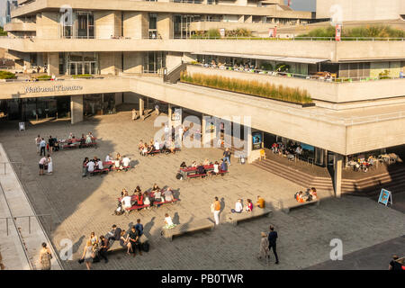 Touristen und Einheimische genießen Sie einen heißen Juli Abend außerhalb der konkreten Brutalist Architektur des National Theatre in London, Großbritannien Stockfoto