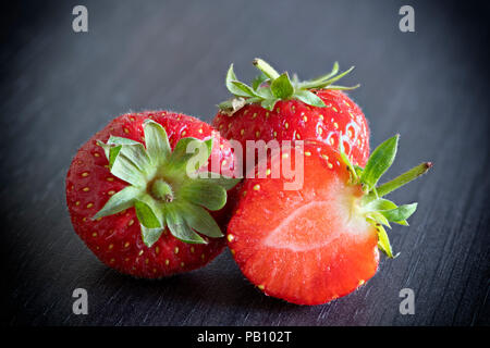 Üppige reife frische Erdbeeren auf einem grauen Küchenarbeitsplatte. Eine Erdbeere in der Hälfte mit saftigen Innenraum Stockfoto