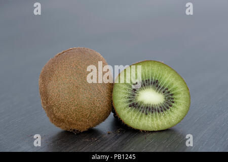 Nahaufnahme eines Ganzen und einer in Scheiben geschnittenen Kiwis auf einer glatten grauen Küchenarbeitsplatte Stockfoto