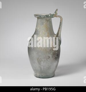 Glaskanne. Kultur: Roman. Abmessungen: 7 7/16 in. (18,9 cm) Andere: 3 5/8 in. (9,2 cm) Durchm. Von rim: 2 3/16 in. (5.6 cm) Durchm. Der Fuß: 2 3/8 in. (6 cm). Datum: Mitte 1.-2. Jh. N.CHR.. One-bearbeitet Krug olpe Form aus Metall ähneln (Bronze) Krüge Transluzent blau grün; Griff und in der gleichen Farbe Trail. Rim ausgeklappt, unten, oben, und heraus, mit abgerundeten Lippe; breite zylindrische Hals nach unten baut unmerklich mit länglichen bauchigen Körper zu verbinden; geringe Integral Basis und konkaver Boden mit unebener Oberfläche; mit zentralen Rippe angewendet wird der Körper mit langen Krallen nach Oben nach Unten Griff, erstellt Stockfoto