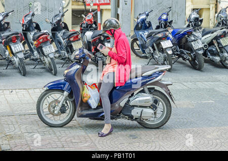 Ho Chi Minh City, Vietnam - 4 April, 2018: Typische Straßenszene - junge Frau auf dem Moped voll mit Helm, maske und handschuhe geschützt, spielen Stockfoto