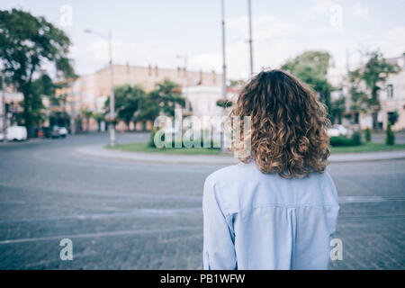 Junge Frau mit dicken lockigen Haar an der europäischen Pflasterstein Ring suchen. Ansicht der Rückseite des unkenntlich Weibliche trägt blaue Shirt ständigen Outsi Stockfoto