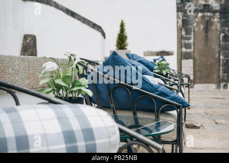 Gemütliche Bänke mit Kissen und eine Anzahl von Blumen für die Dekoration auf einer Terrasse an der Straße oder in einem Cafe. Gemütliche Lage zum Entspannen an der frischen Luft. Stockfoto