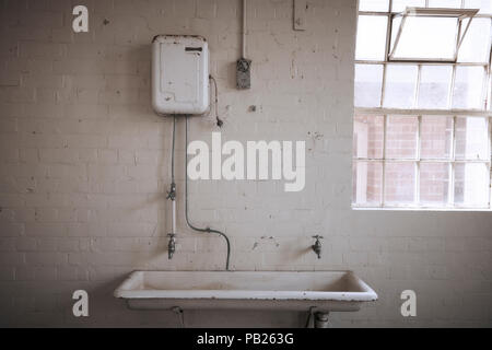 Alten, verlassenen heißes Wasser Service über ein großes, weißes Porzellan Waschbecken in einem weißen Stein Zimmer. Stockfoto