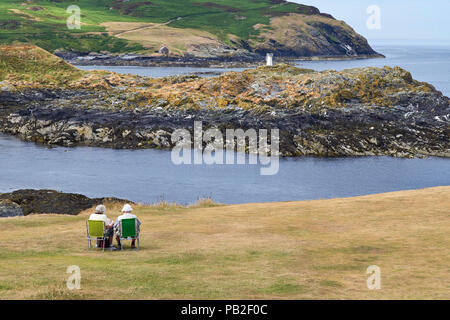 Älteres rentnerehepaar Lesen der Papiere während der Sitzung auf der Insel Man mit Blick auf die Wade Mann Stockfoto