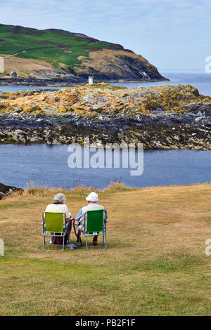 Älteres Ehepaar in perfekter Ort sitzen am Sound, von der Insel Man mit Blick auf das Kalb des Menschen Zeitung lesen Stockfoto