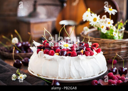 Köstliche Pavlova baiser Kuchen mit frischen Himbeeren und Kirschen auf rustikalen Hintergrund eingerichtet Stockfoto