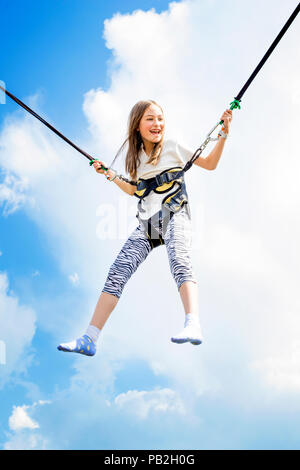 Kleines Mädchen springt hoch in die Luft mit einem Bungee Trampolin. Stockfoto