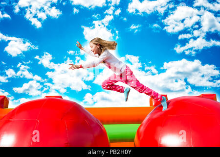 Gerne kleine Mädchen haben viel Spaß beim von Ball zu Ball springen auf ein Schloss aufpumpen. Stockfoto
