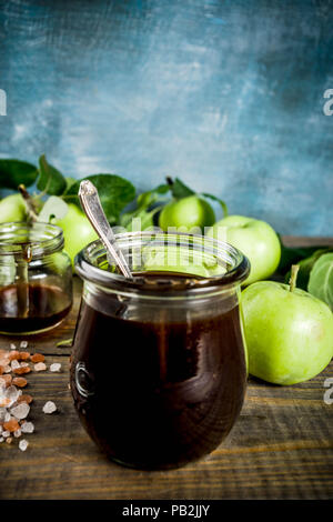 Home Warme dunkle gesalzen classic Karamell-sauce, mit grünen Äpfeln, Holz- und dunkelblauen Hintergrund, Stockfoto