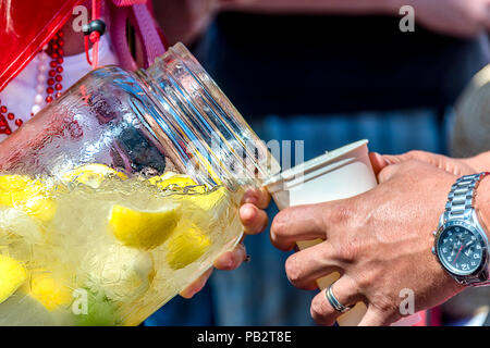 Frau in Perlen gießt kaltes Wasser mit Eis und geschnitzten Zitronen aus einem Glas Flasche in ein Glas für Menschen, die mit einem Ring und eine Uhr auf der Hand Stockfoto