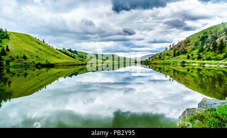 Dunkle Wolken und die umliegenden Berge im Wasser von Trapp See widerspiegelt, entlang der Autobahn 5 zwischen Kamloops und Merritt im schönen BC Kanada Stockfoto