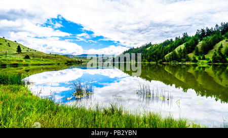 Blauer Himmel, Wolken und die umliegenden Berge im Wasser von Trapp See widerspiegelt, entlang der Autobahn 5 zwischen Kamloops und Merritt im schönen BC Kanada Stockfoto