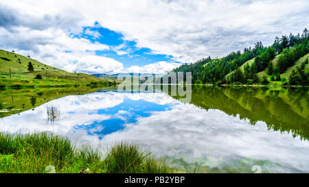 Blauer Himmel, Wolken und die umliegenden Berge im Wasser von Trapp See widerspiegelt, entlang der Autobahn 5 zwischen Kamloops und Merritt im schönen BC Kanada Stockfoto