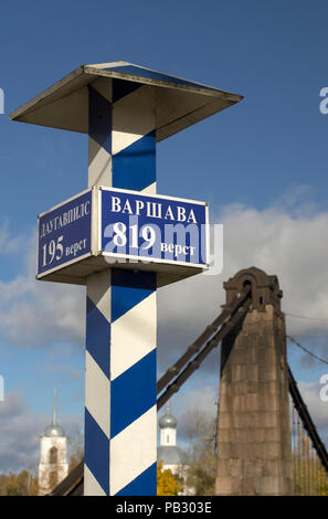 Milepost mit Namen der Städte in der Russischen und der Entfernung in Kilometern und die Säulen der Suspension Bridge im Hintergrund Stockfoto