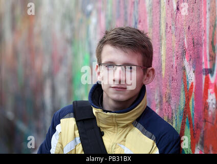 Junge schöne Junge mit Brille in der Stadt auf dem Hintergrund einer bunten Wand. Stockfoto