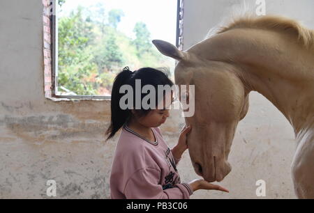 (180726) - NANCHANG, 26. Juli 2018 (Xinhua) - Tang Siqi, ein Schüler von Sonnenschein, Reitschule, interagiert mit einem Pferd in Yihuang Grafschaft von Fuzhou, der ostchinesischen Provinz Jiangxi, 15. März 2018. Pferdesport nie in Yihuang, eine landwirtschaftliche Grafschaft in der ostchinesischen Provinz Jiangxi gehört, bis Sonnenschein Reitschule begann Recruiting ländliche Jugendliche im Jahr 2015. Bisher haben die meisten der 90 Schüler arbeiten oder angehende im Pferd zur Arbeit reiten Vereine in Chinas größten Städten wie Peking, Shanghai und Hangzhou. (Xinhua / Zhou Mi) (lmm) Stockfoto